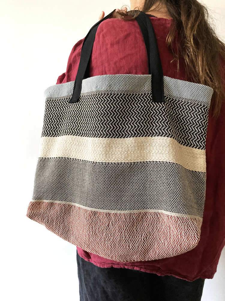 A handmade woven handbag in red, brown, black & white with cloth straps (handles). The bag was woven with cotton & wool yarns